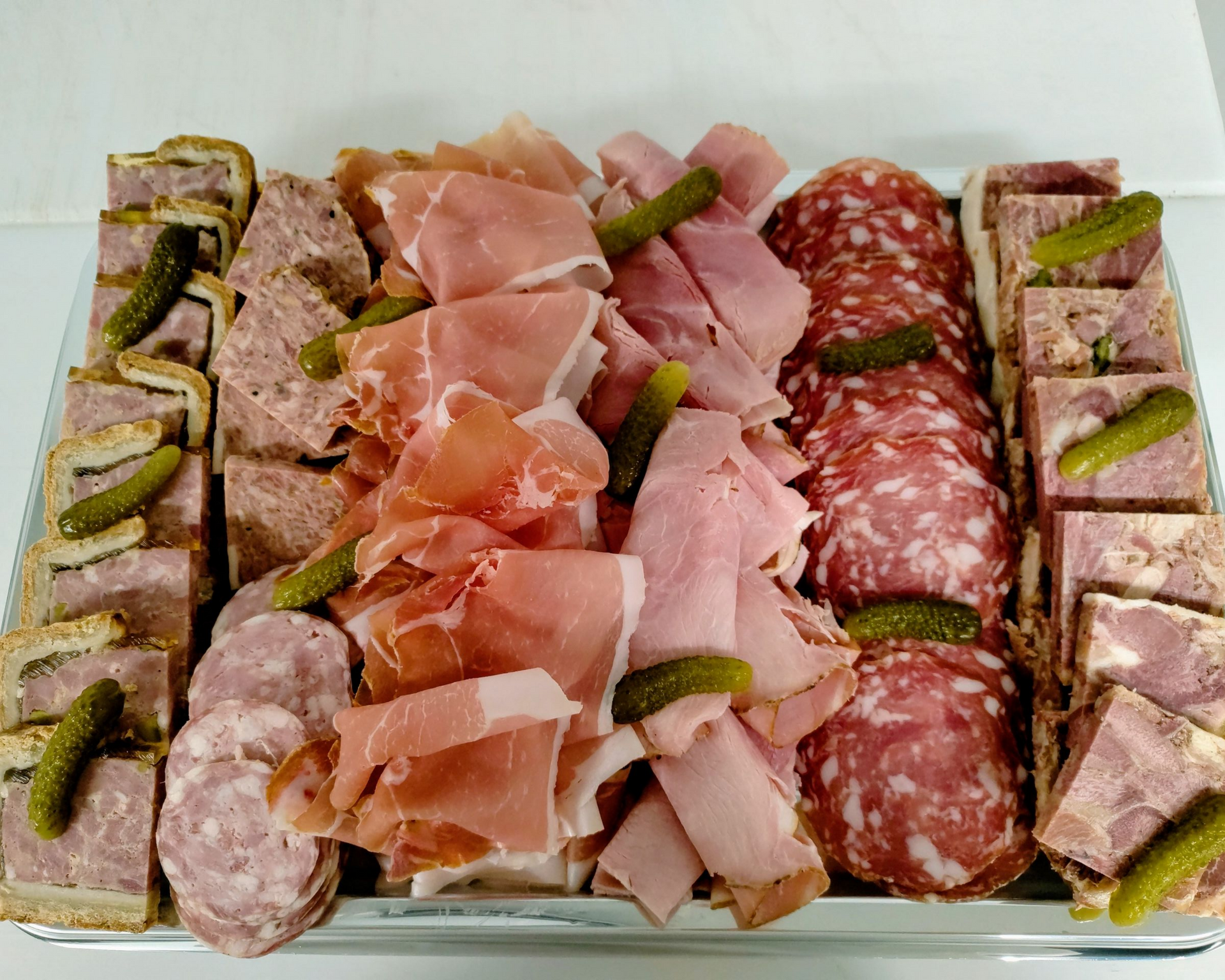 Assortiment de charcuteries avec des viandes tranchées, des fromages et des cornichons disposés sur un plateau.