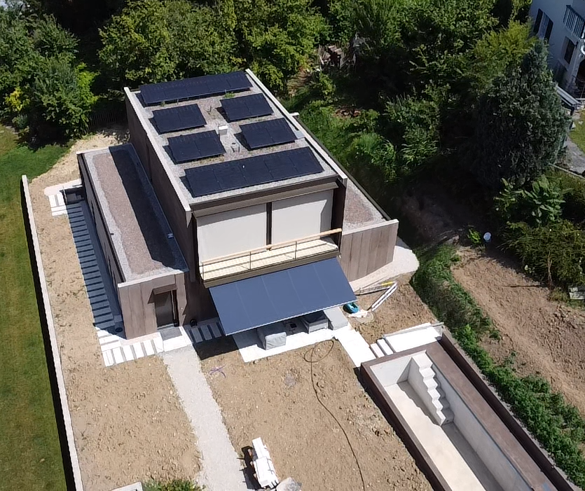 Modernes Haus mit Solarmodulen auf dem Dach, einem Gehweg und einem Pool. Bäume umgeben das Haus.