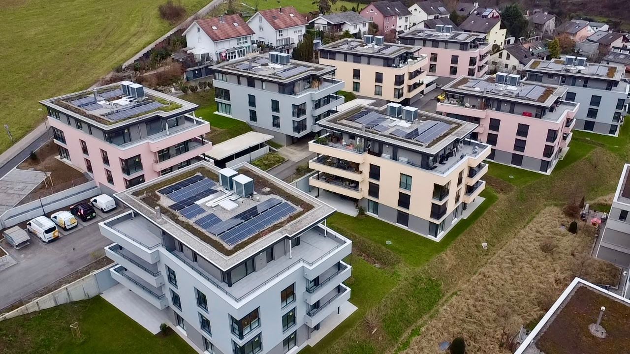 Eine Luftaufnahme moderner, mehrstöckiger Wohnanlagen mit Solarmodulen auf einem grasbewachsenen Hügel.