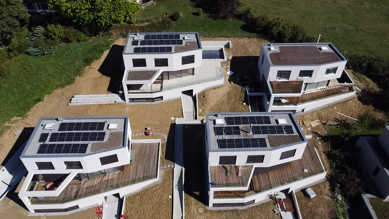 Luftaufnahme von vier modernen weißen Häusern mit Solarmodulen auf den Dächern.