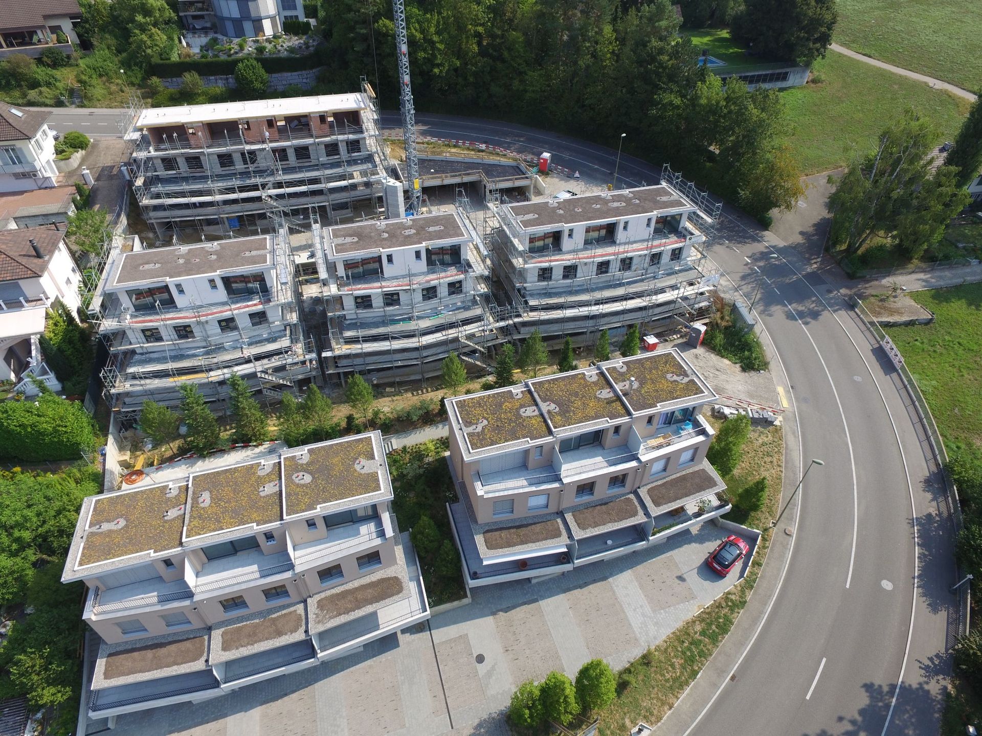 Luftaufnahme mehrerer im Bau befindlicher mehrstöckiger Wohnhäuser in der Nähe einer kurvigen Straße.