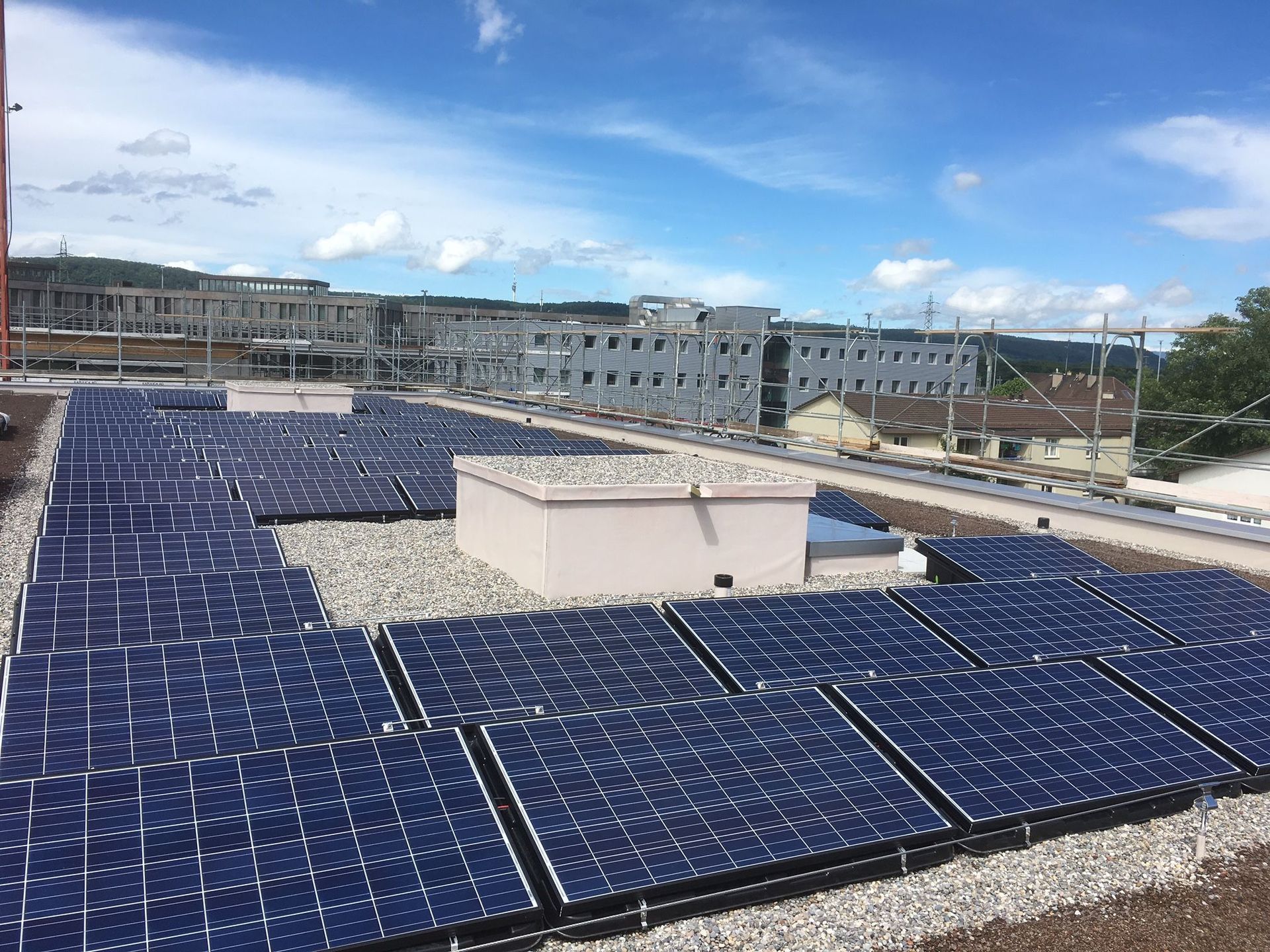An einem sonnigen Tag bedecken Solarmodule ein Flachdach mit Gebäuden im Hintergrund.