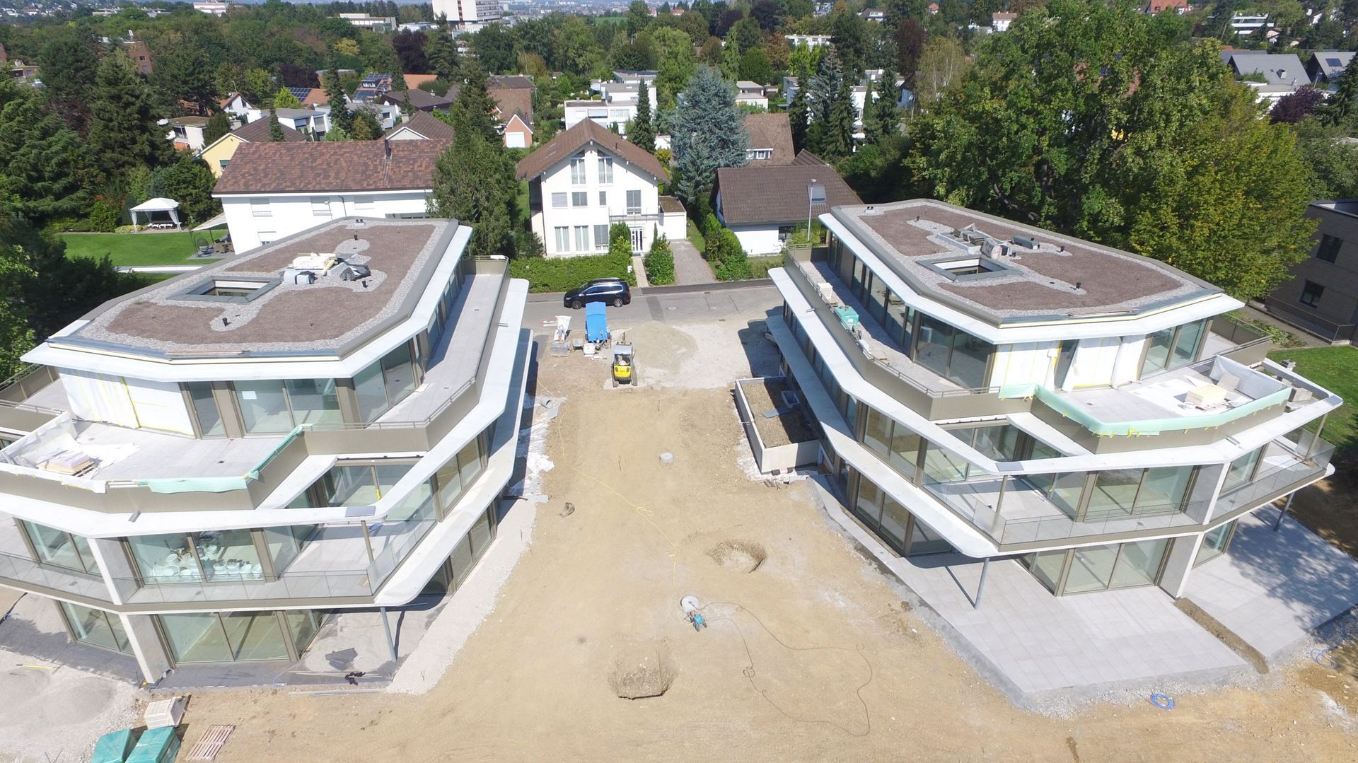 Luftaufnahme von zwei im Bau befindlichen modernen Wohnhäusern, umgeben von Bäumen und Häusern.