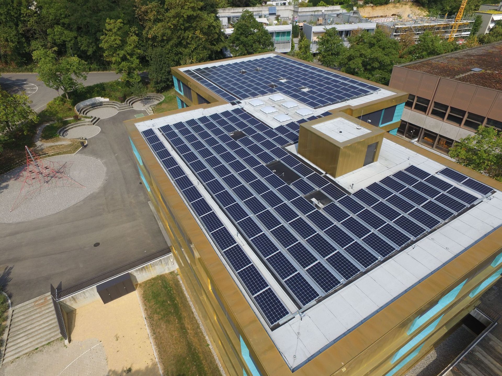 Solarmodule auf einem Schuldach erzeugen erneuerbare Energie. Sonniger Tag, blaue Module, Gebäude im Hintergrund.