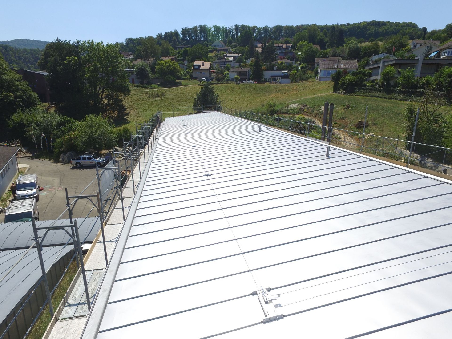 Metalldach mit Wellenmuster mit Blick auf einen grünen Hügel mit Häusern unter blauem Himmel.