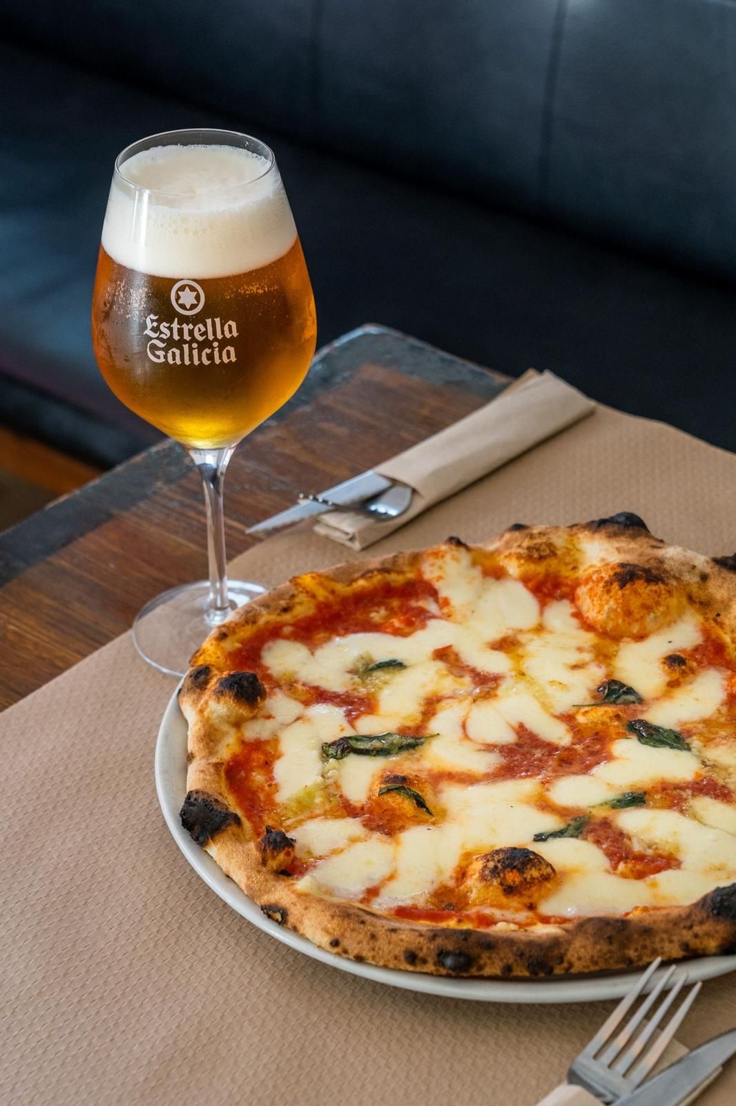 Pizza y cerveza: Una pizza Margherita reposa junto a un vaso de cerveza Estrella Damm sobre una mesa.