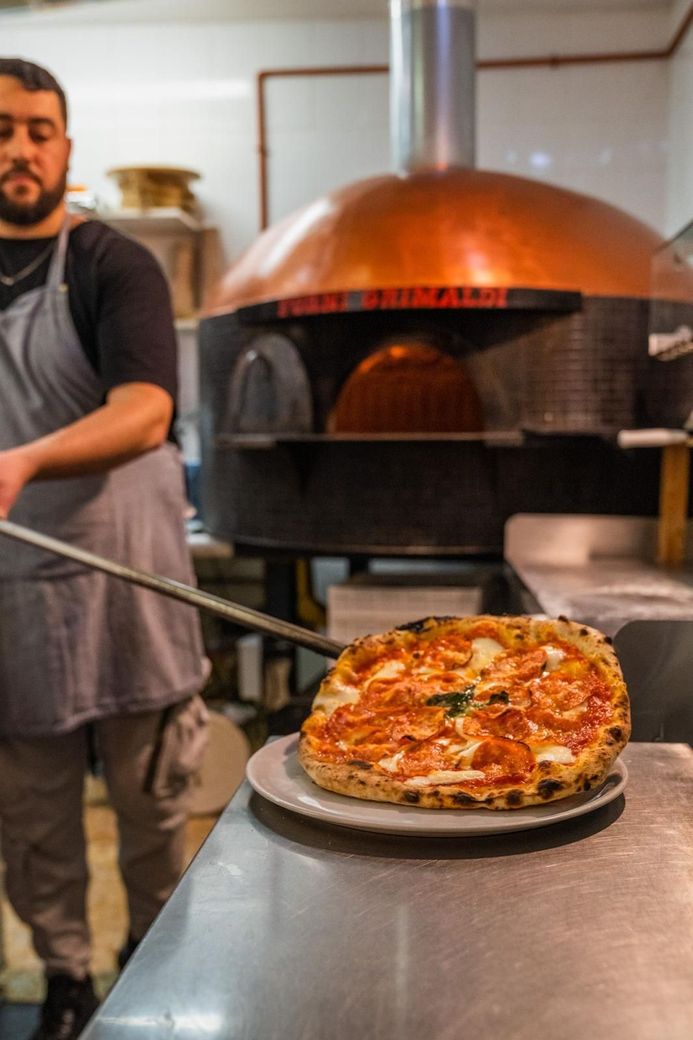 Un chef saca una pizza del horno de cobre en una cocina.