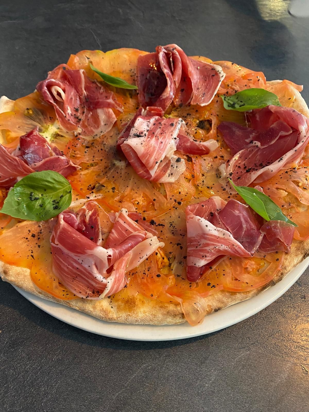 Pizza con prosciutto y albahaca, en plato blanco.