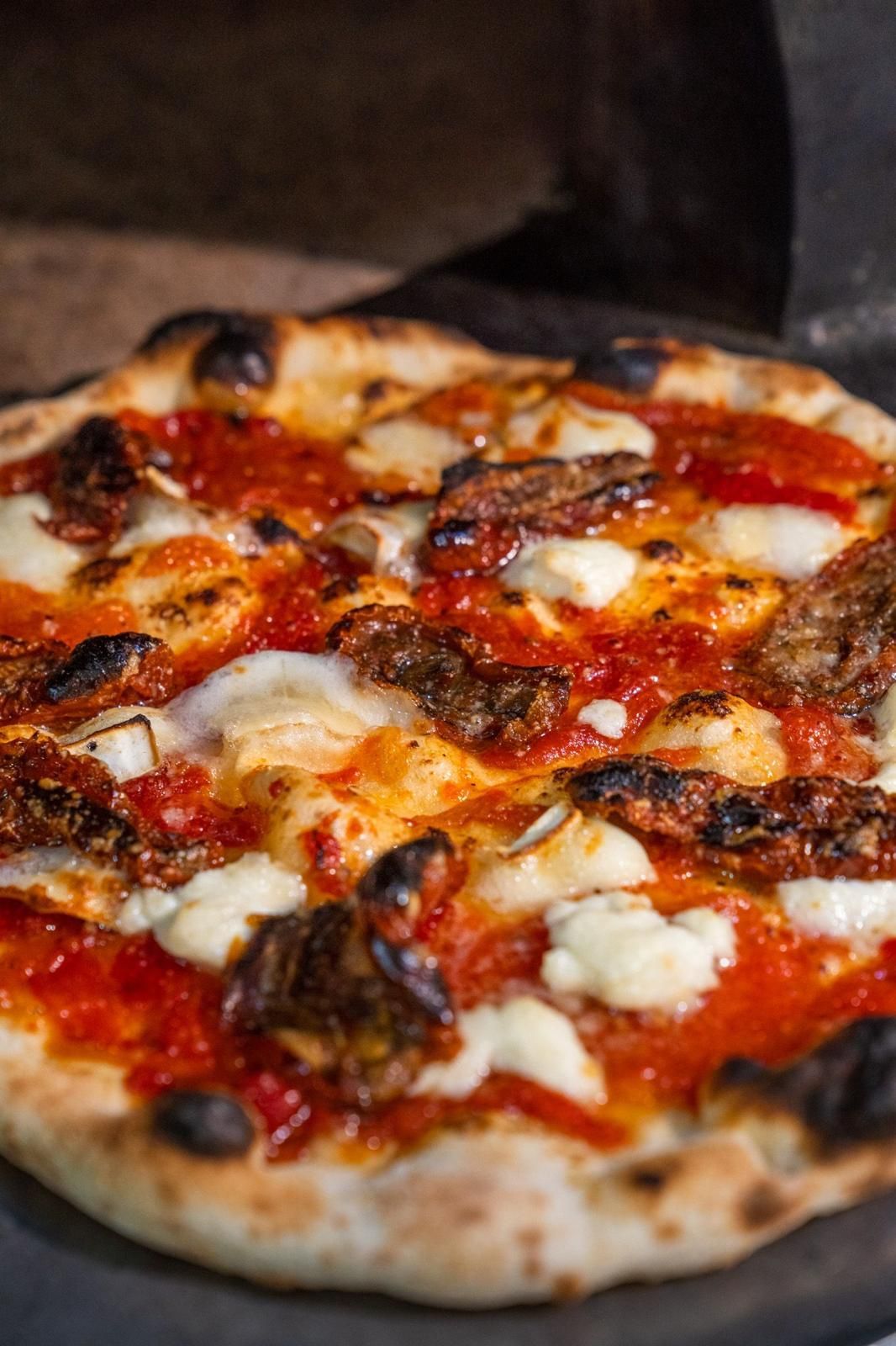 Pizza con salsa roja, mozzarella y aderezos oscuros horneándose en el horno.
