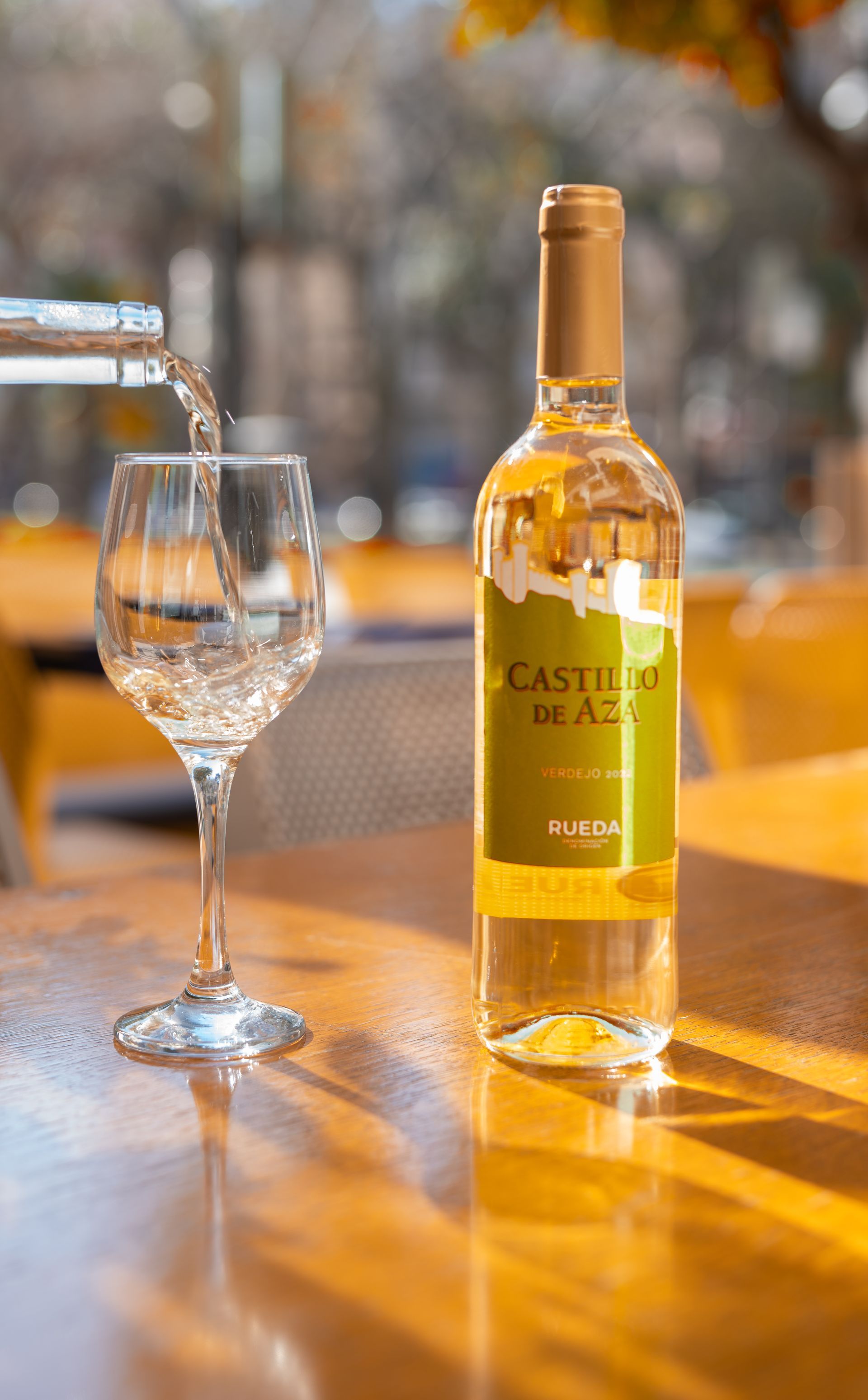 Vino vertido en una copa junto a una botella de vino blanco