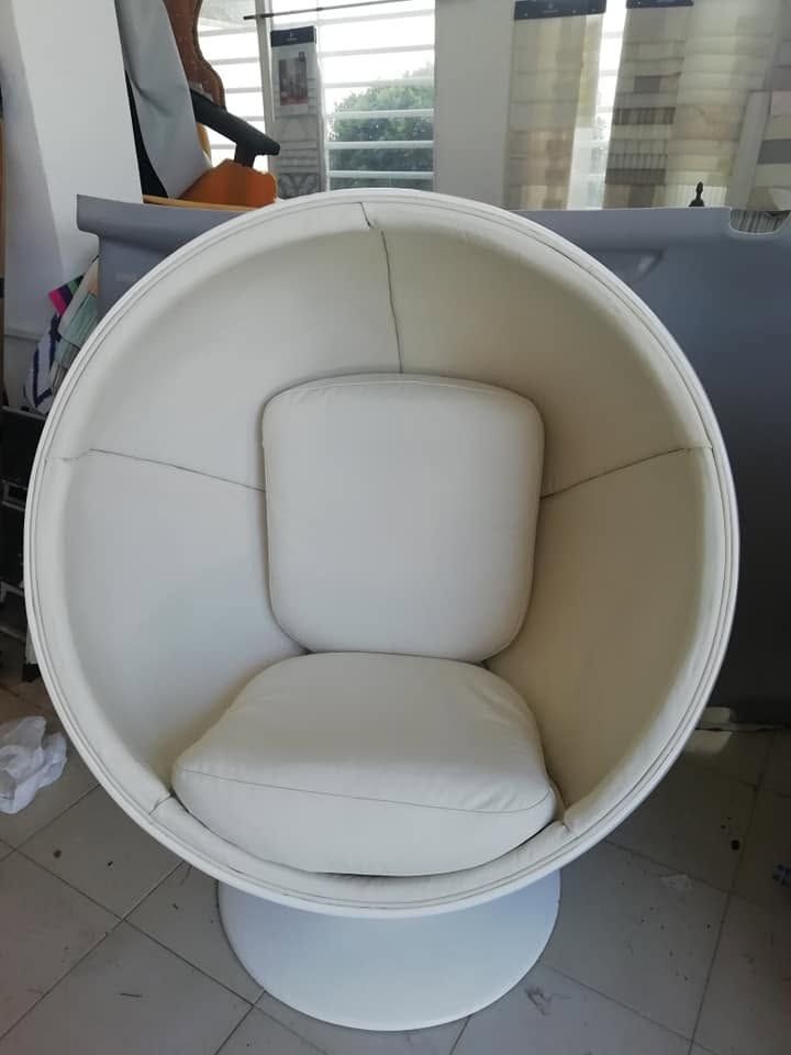 Sillón blanco con forma de huevo y cojín beige en una habitación luminosa, cerca de una ventana.