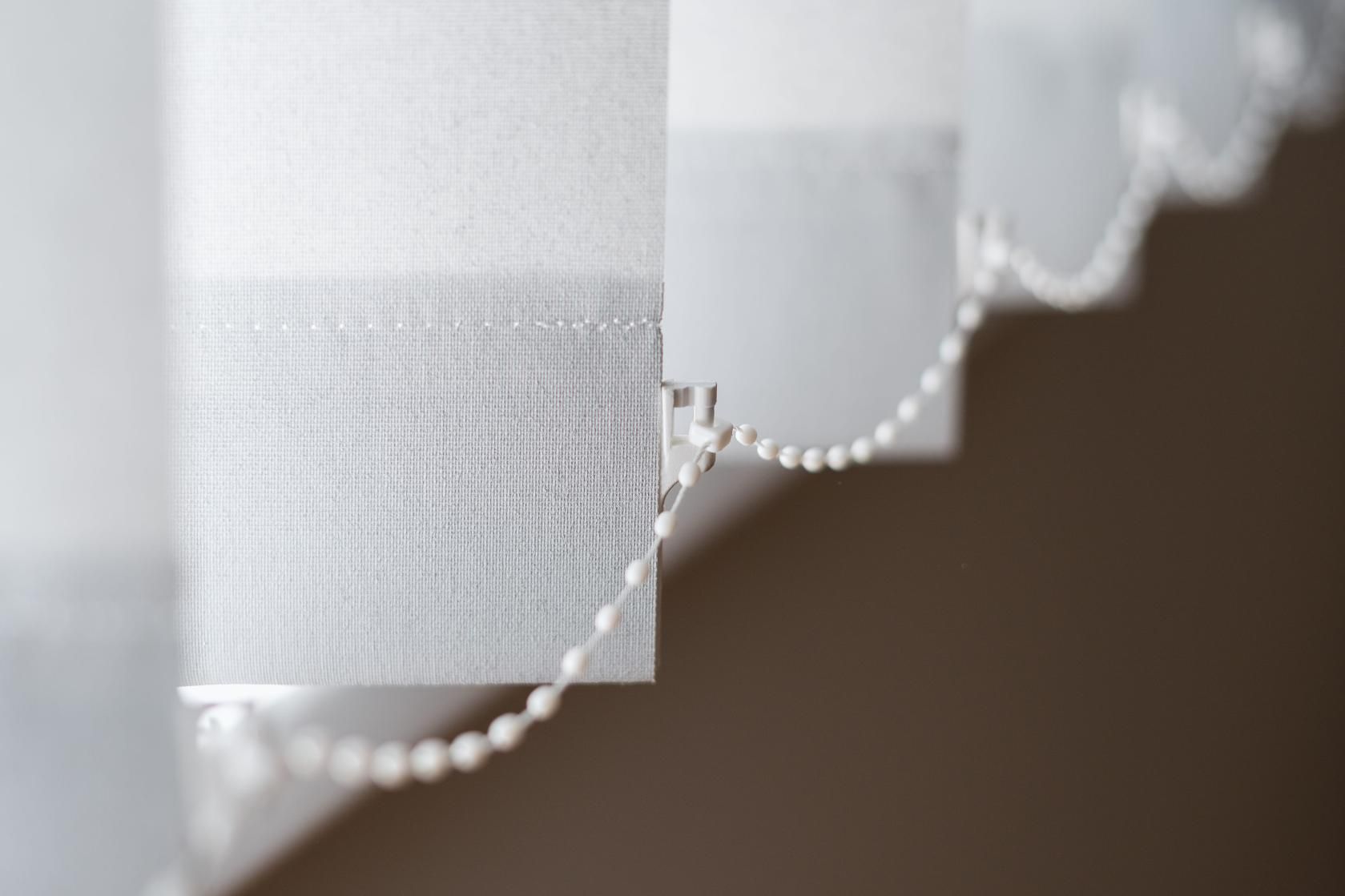Cortinas blancas transparentes con un borde festoneado adornado con cuentas sobre un fondo marrón.