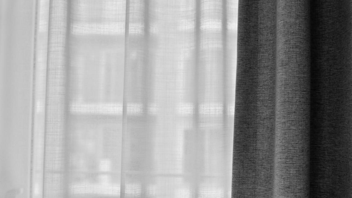 Cortinas blancas transparentes junto a una cortina gris oscuro frente a una ventana.