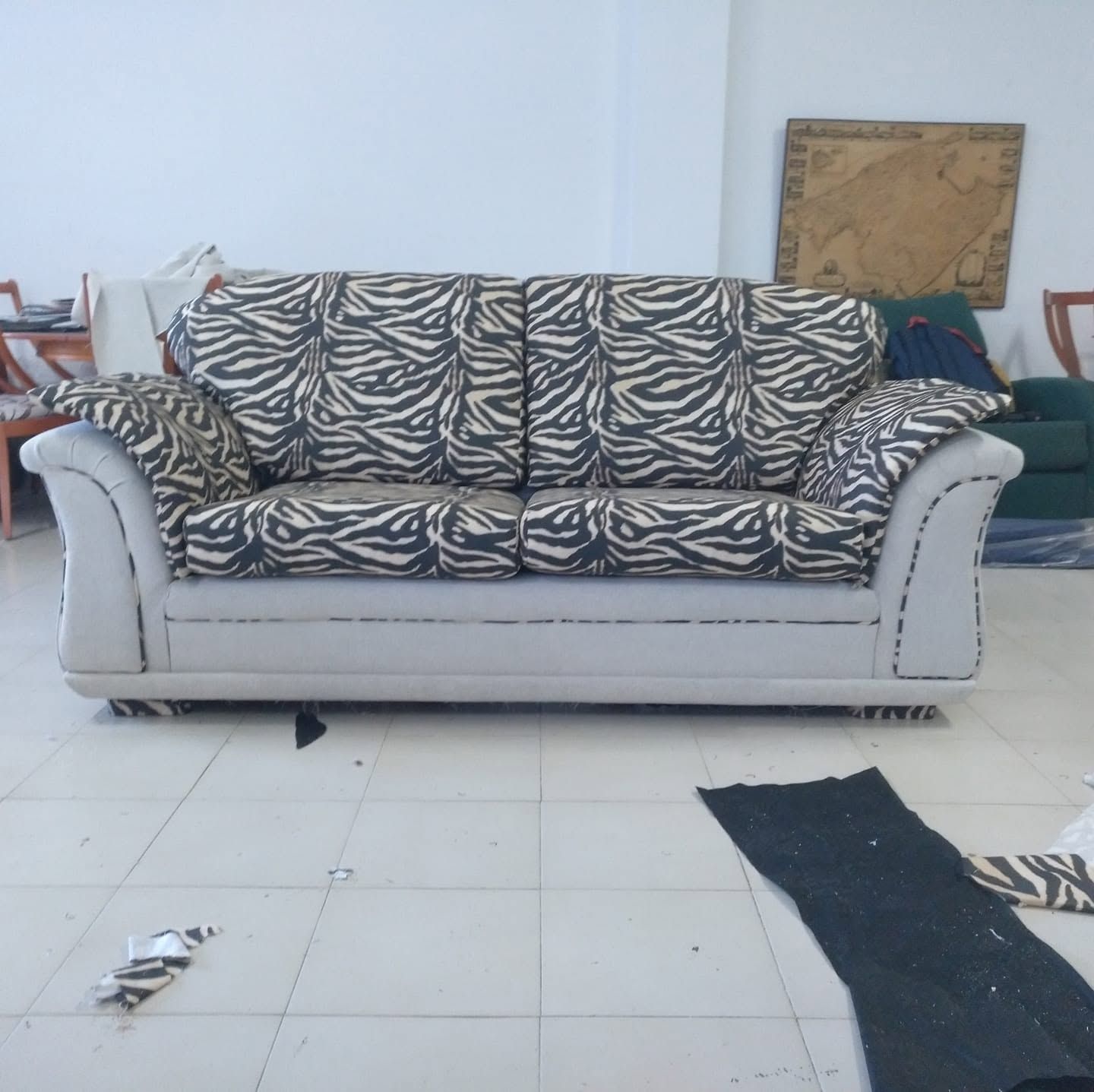 Sofá con estampado de cebra en una habitación luminosa con suelo de baldosas y algunos objetos esparcidos por el suelo.