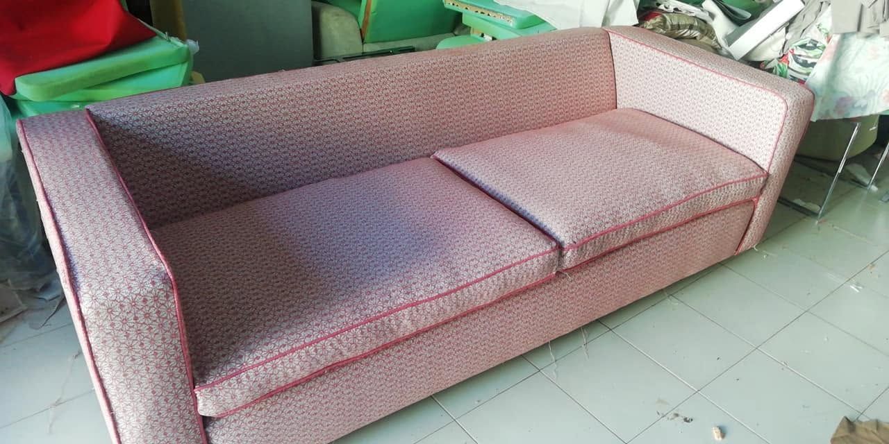 Sofá tapizado rosa con dos cojines en una habitación con suelo de baldosas.
