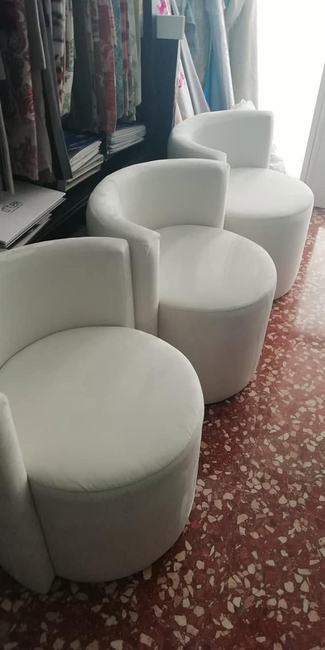 Una hilera de otomanas redondas blancas junto a estanterías sobre un suelo estampado cerca de una ventana luminosa.