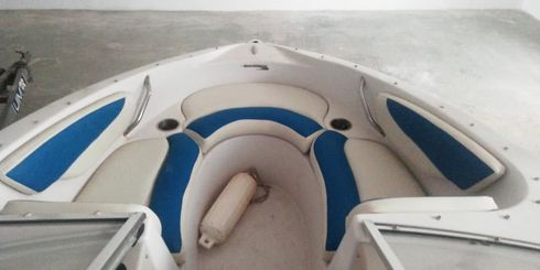 Proa de un barco blanco con cojines azules en aguas tranquilas.