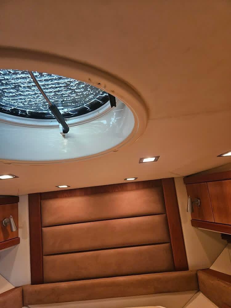 Interior de una cabina de barco con tapicería color canela, revestimiento de madera y una claraboya redonda en el techo.