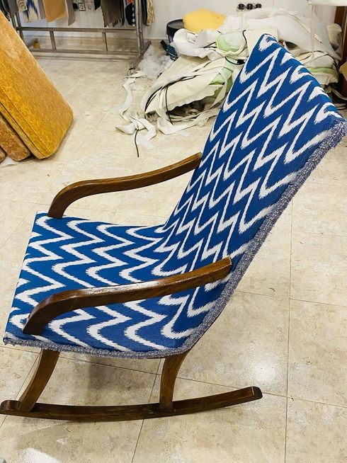 Mecedora azul con estampado en zigzag y brazos de madera sobre un suelo claro, en una habitación desordenada.