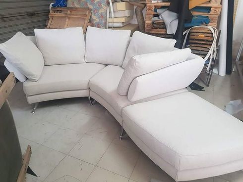 Sofá modular blanco en una sala de exposición de muebles, con cojines y una chaise longue tipo otomana.