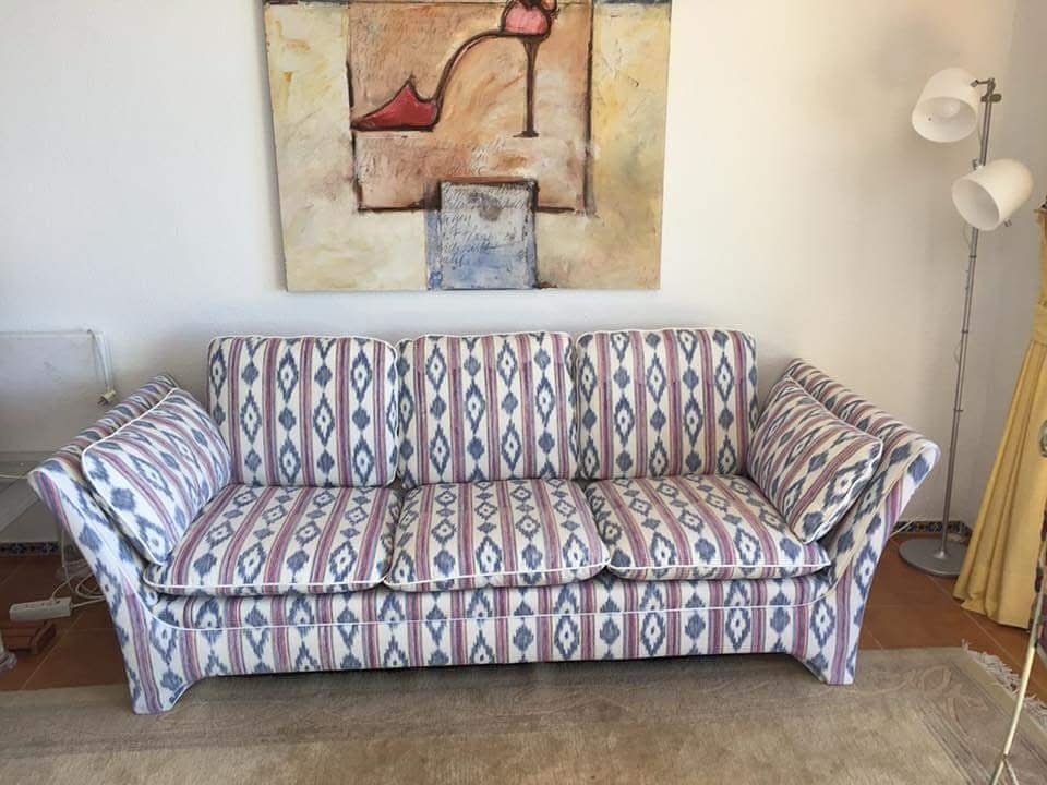 Sofá estampado en una sala de estar con cuadros en la pared y una lámpara de pie.