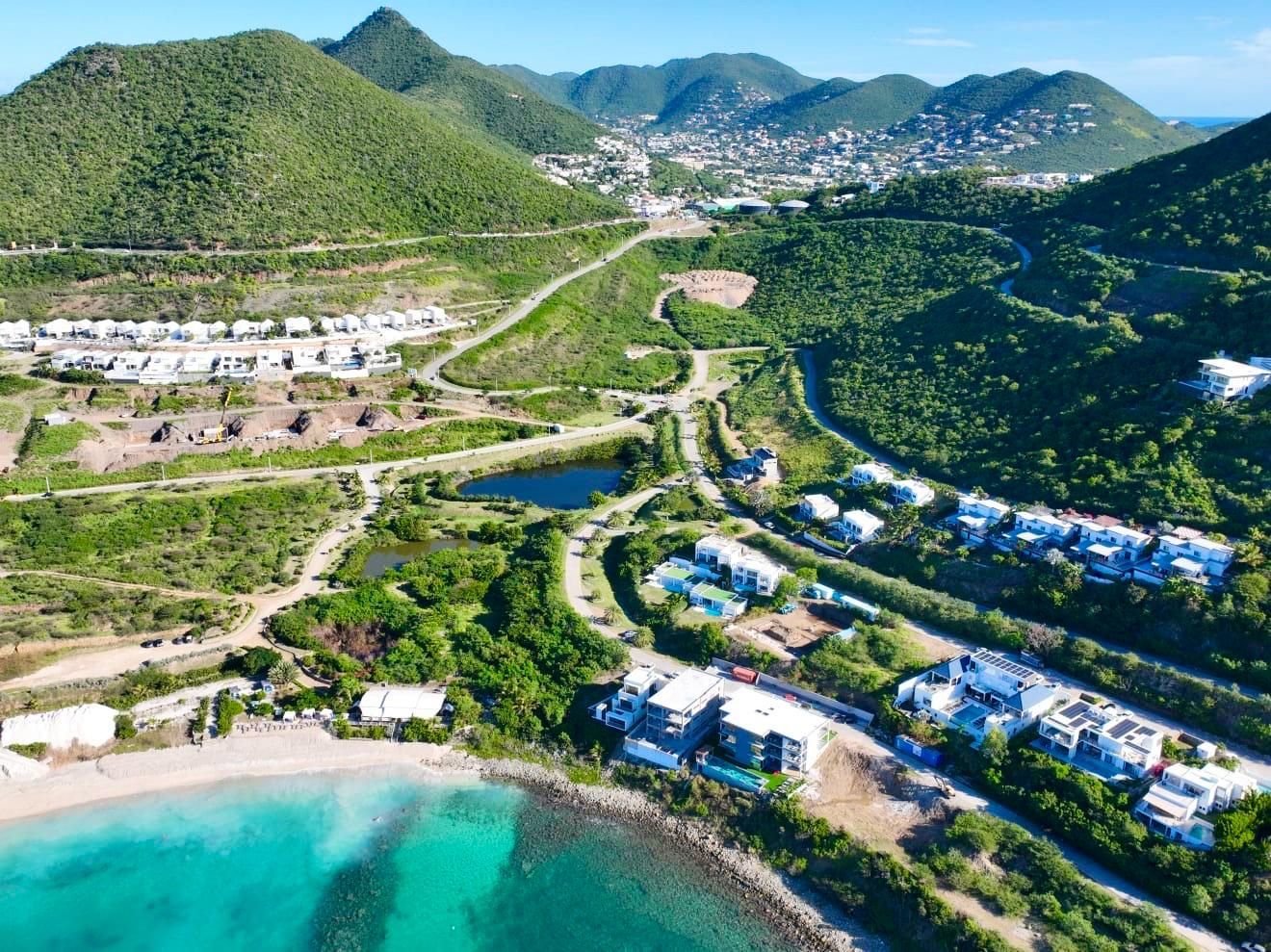 Coastal view: turquoise water, white buildings, green hills, houses nestled in mountainside, bright sunny day.