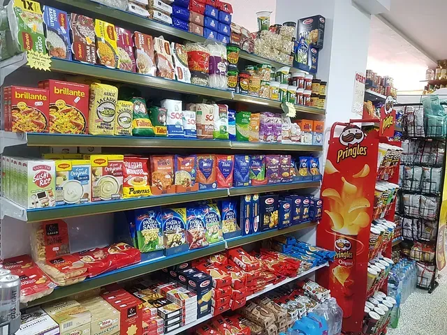 Estantes de una tienda de comestibles llenos de diversos alimentos envasados, incluidos pastas, bocadillos y patatas fritas.