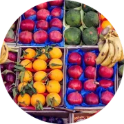 Exhibición de frutas: naranjas, granadas, sandías y plátanos en cajas.
