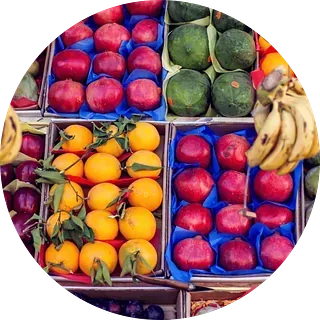 Exhibición de frutas: naranjas, granadas, sandías y plátanos en cajas.