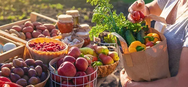 Persona con una bolsa de papel llena de productos frescos de un mercado agrícola. Diversas frutas y verduras en exposición.