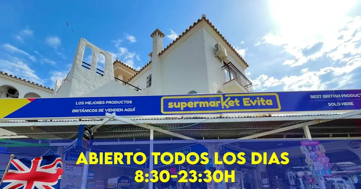 Supermercado Evita con cartel azul, abierto todos los días 8:30-23:30H, edificio blanco detrás, bandera Union Jack.