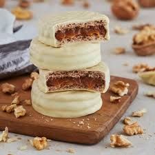 Pila de alfajores de chocolate blanco sobre una tabla de madera, rodeada de nueces.