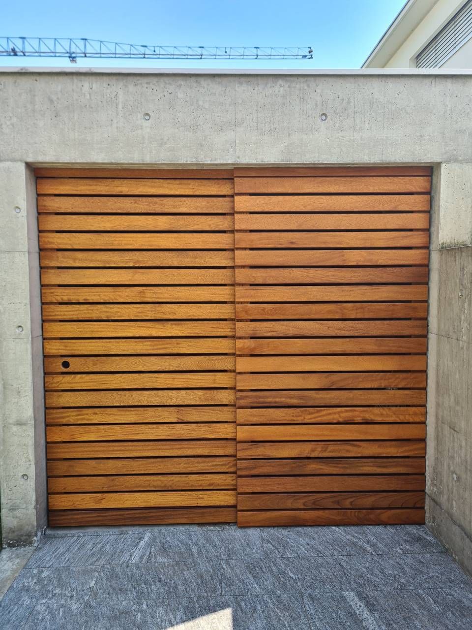 Porte da garage con doghe orizzontali in legno, fissate al cemento, contro un cielo azzurro.