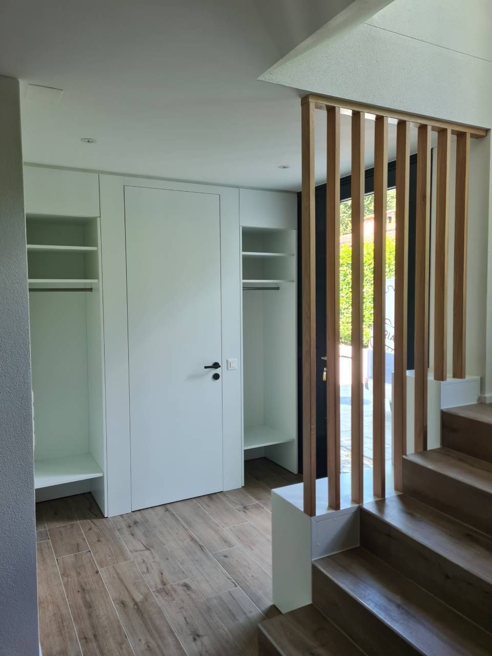 Armadio bianco con ripiani aperti e aste appendiabiti, accanto a una ringhiera in doghe di legno per le scale.