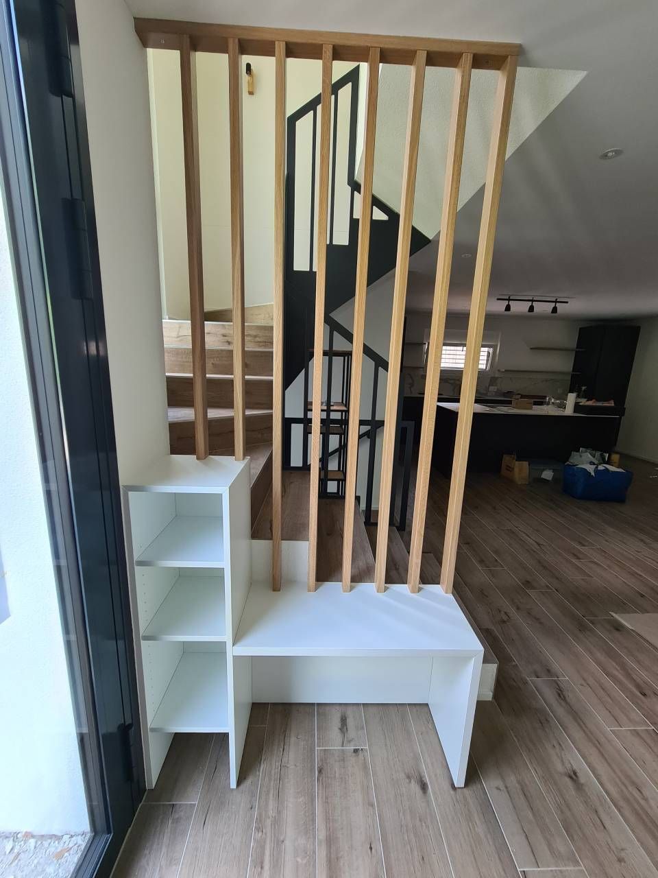 Mobile contenitore bianco e paravento in doghe di legno davanti alle scale, ambiente interno.