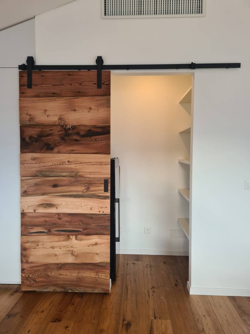 Porta del fienile in legno, aperta su una dispensa con ripiani bianchi e pavimenti marroni.