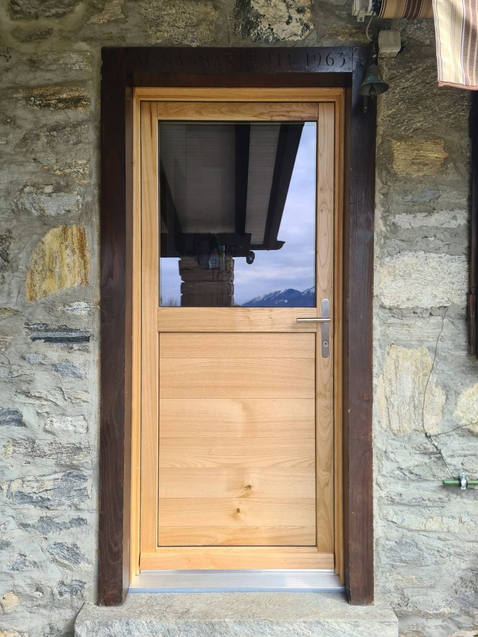 Porta in legno con pannello in vetro incastonato in un muro di pietra. Cornice marrone scuro attorno alla porta.