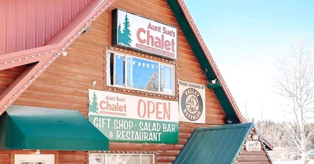Sign for Aunt Sue's Chalet, a gift shop and restaurant, with a green awning and snow.