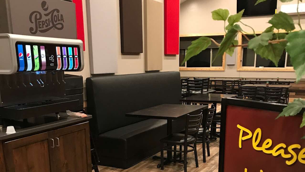 Restaurant interior with black booth seating, soda fountain, and empty tables.