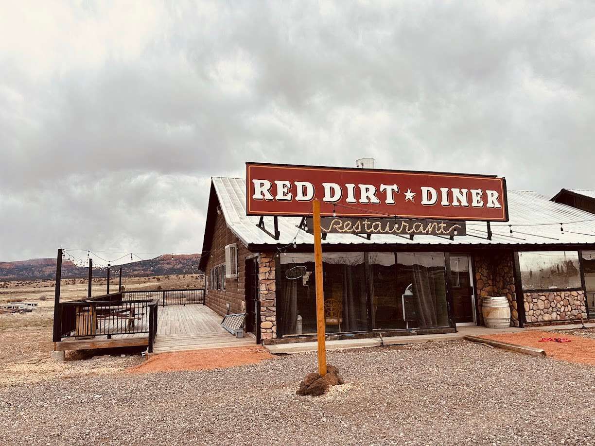 Red Dirt Diner with red sign, brown building, gravel lot, and cloudy sky.