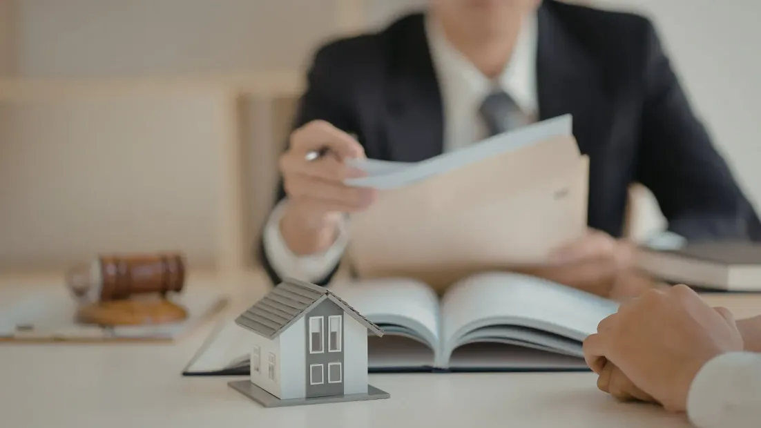 Abogado presentando documentos a un cliente, modelo de casa sobre mesa.