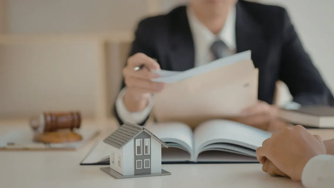 Abogado presentando documentos a un cliente, modelo de casa sobre mesa.