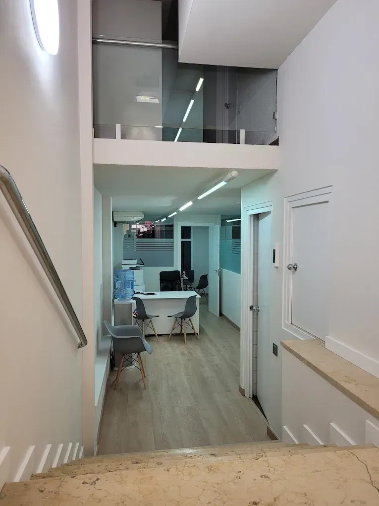 Escalera que conduce a una oficina con paredes blancas, pisos de madera y un escritorio.