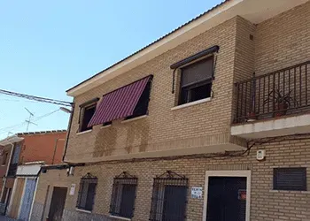 Un edificio de ladrillo con un balcón y un toldo rojo en las ventanas.