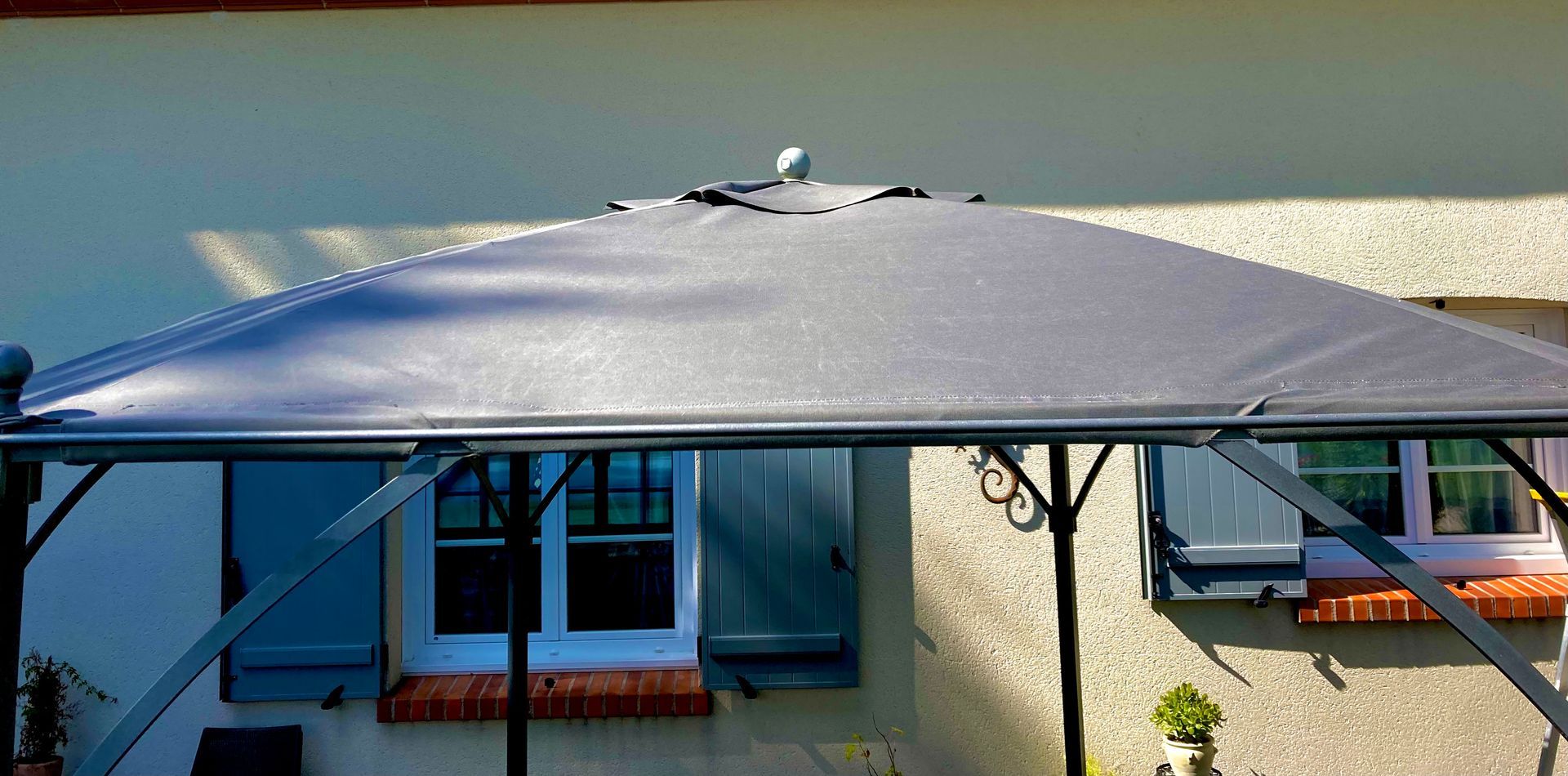 Une structure de toit de gazebo gris foncé est placée devant une maison.