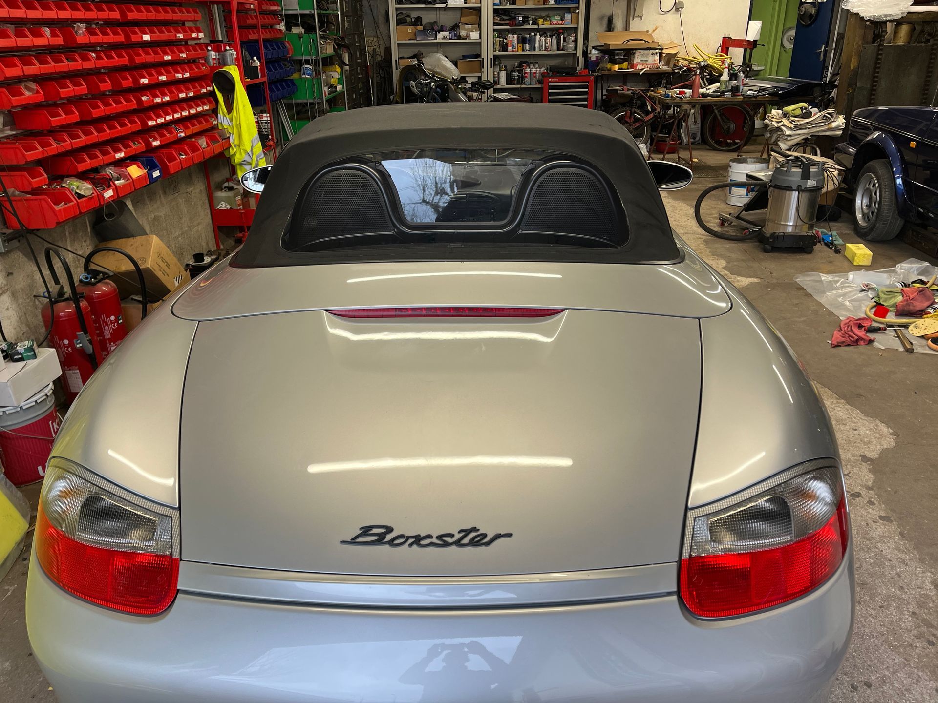 Vue arrière d'une Porsche Boxster cabriolet argentée garée dans l'atelier d'un garage.