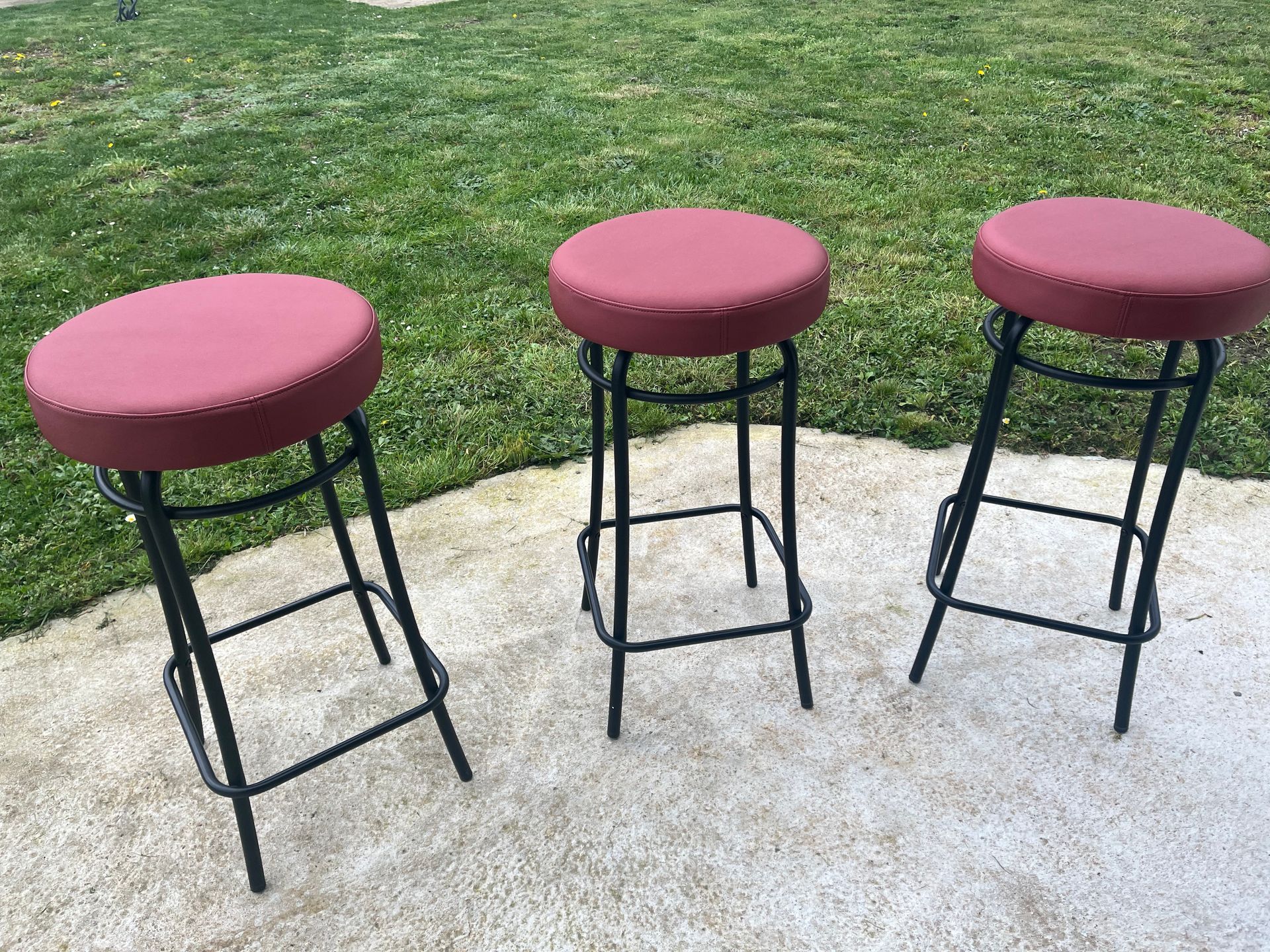 Trois tabourets de bar à structure métallique noire et assises rondes rembourrées rose rougeâtre.