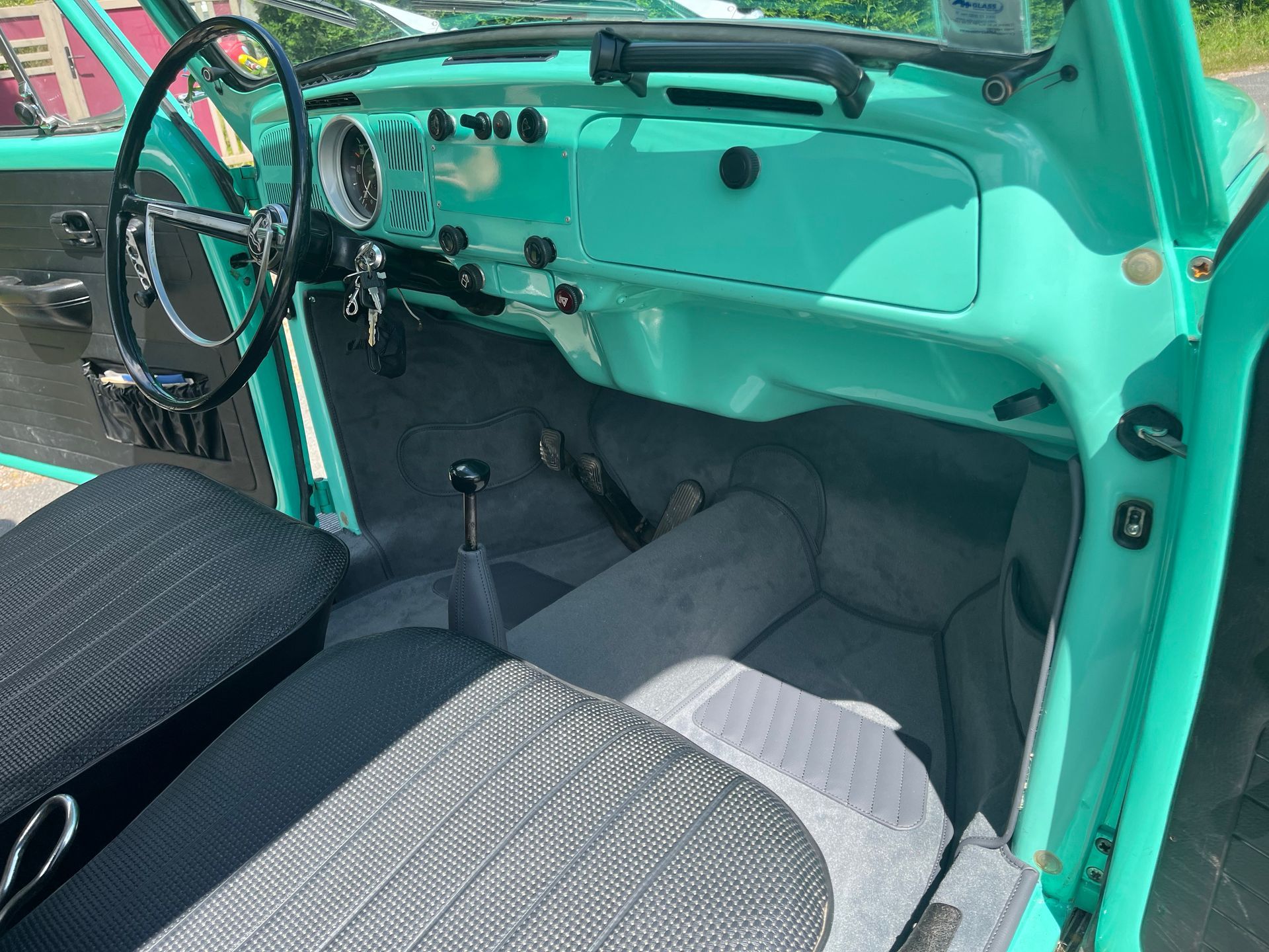 L'intérieur d'une Volkswagen Beetle bleu turquoise vif, montrant le volant, le tableau de bord et les sièges en tissu gris.