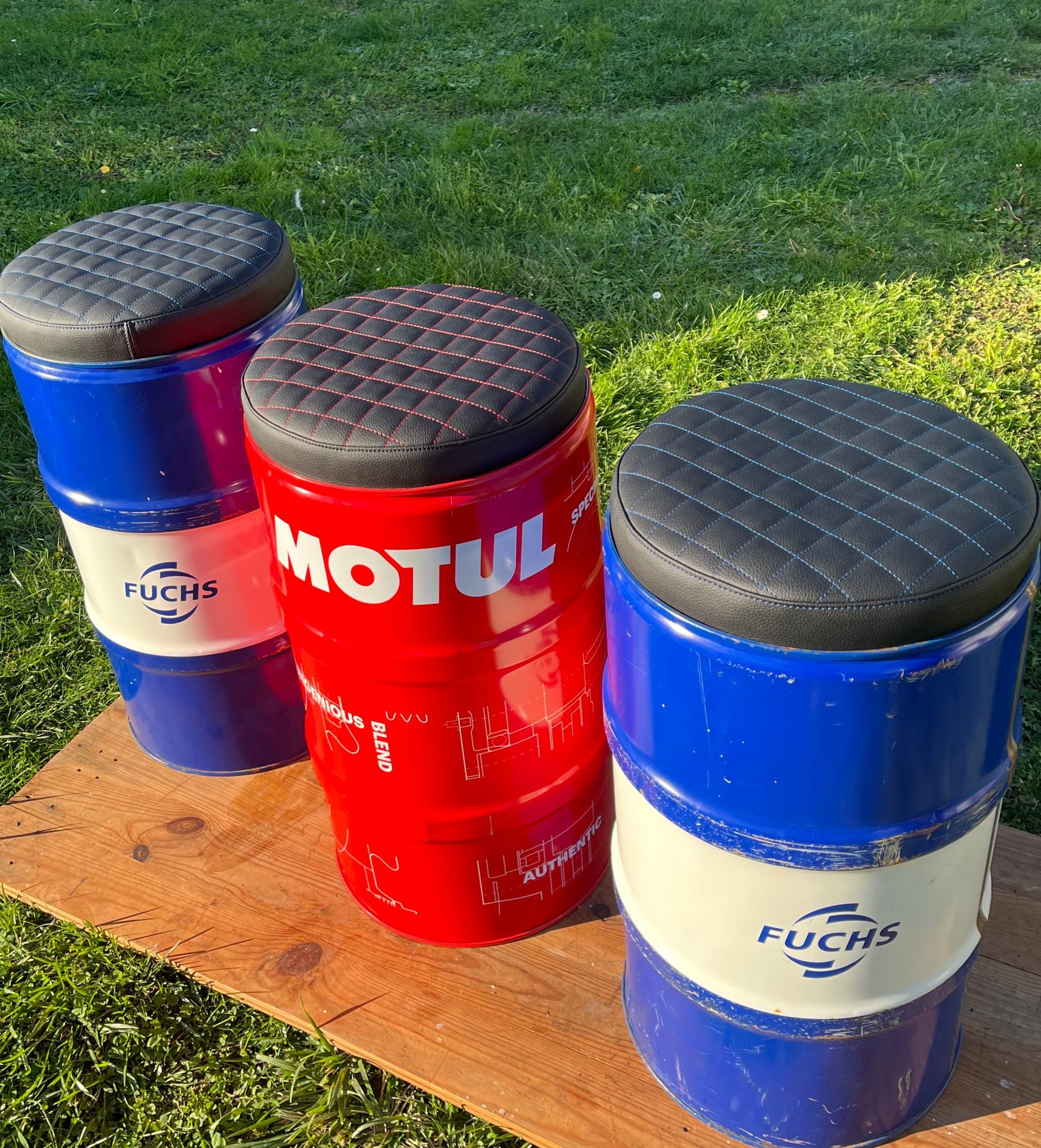 Trois tabourets en métal fabriqués à partir de fûts d'huile, avec des coussins noirs matelassés.