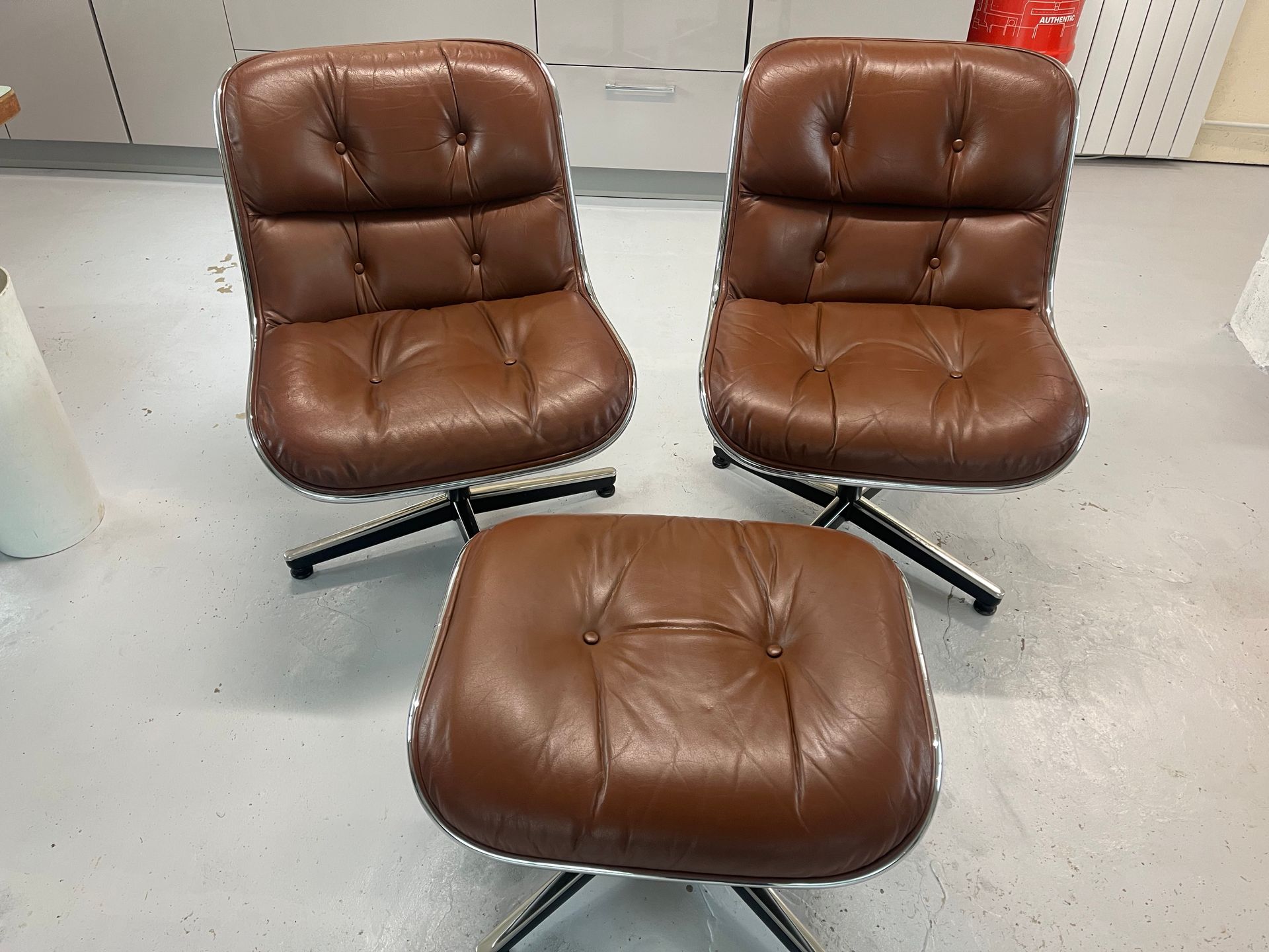 Deux fauteuils pivotants en cuir marron et un pouf assorti sur un sol clair.